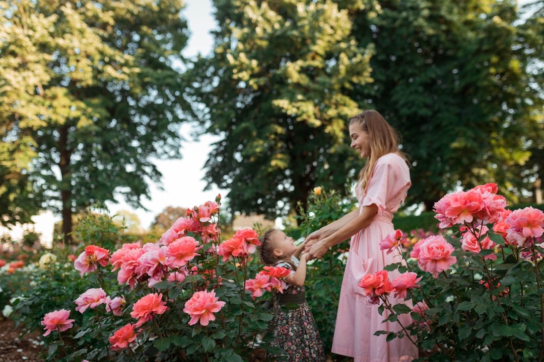 Mother and daughter holding hands and walking together through a garden of pink roses