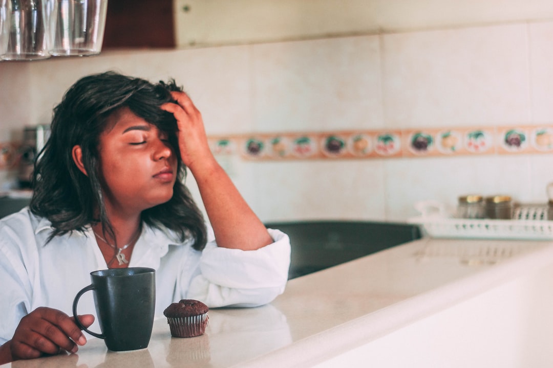 Tired mom resting her head in her hand next to a cup of coffee in the morning