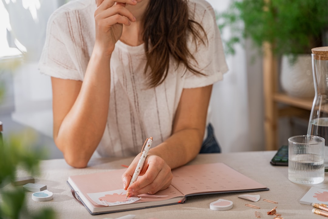 A mom sitting down at a bright kitchen table, writing out her overloaded fall calendar