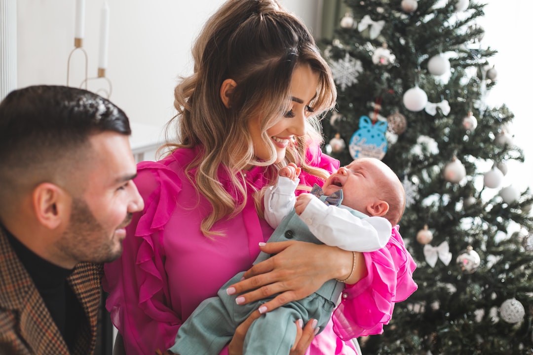 New mom and dad holding their baby together beside the Christmas tree, her first Christmas as a mom