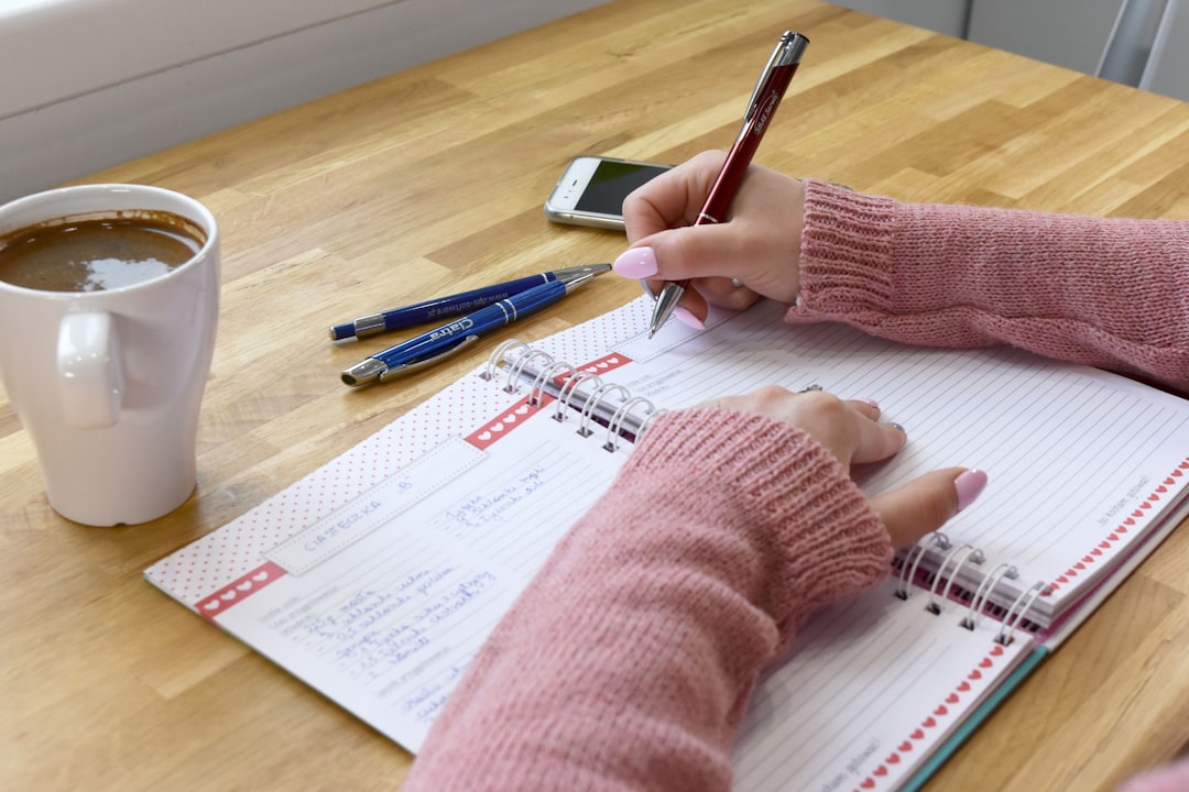 A woman in a cozy sweater handwriting a family recipe in a notebook with coffee nearby